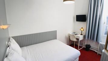 A hotel room with a bed, a desk, a chair, a lamp, a TV, and a window with curtains.