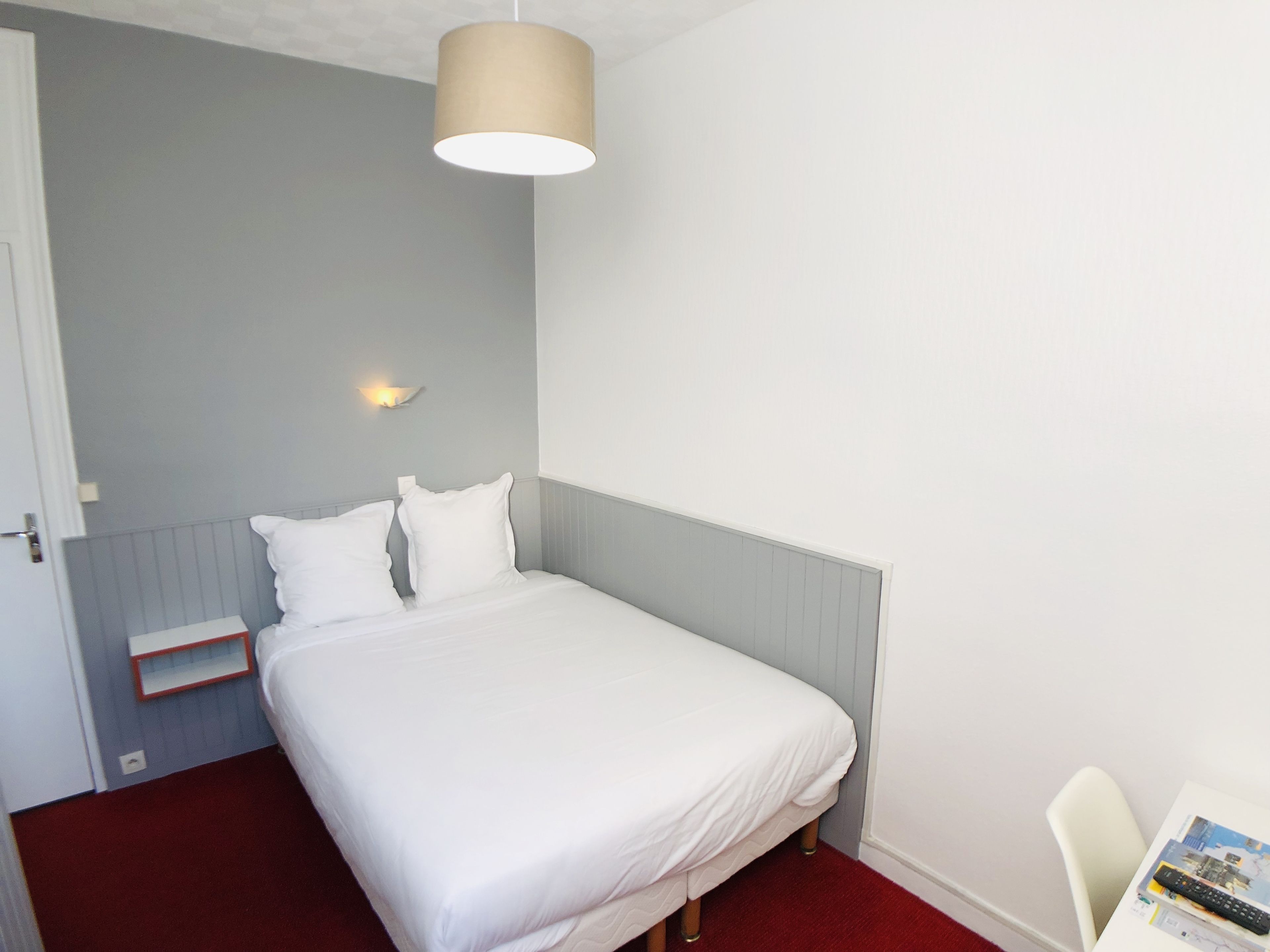 A neatly made bed in a room with a light blue wall, a white bedside table, and a hanging lamp.