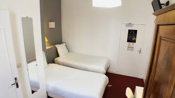 A hotel room with two single beds, a desk, a chair, a wardrobe, and a door with a poster.