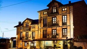 A multi-story building with a traditional architectural style, featuring a balcony on the second floor and a visible entrance with a door and steps. - Posada Santa Ana (Suances)
