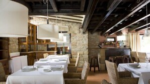 A restaurant with stone walls, wooden beams, and wicker furniture. Tables are set with white tablecloths and plates. - Posada Santa Ana (Suances)