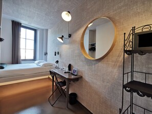 Een moderne hotelkamer met een bed, bureau, stoel en een grote spiegel.
