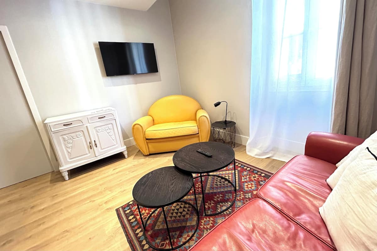 A modern living room with a yellow sofa, a red couch, a TV mounted on the wall, and a small side table with a lamp.