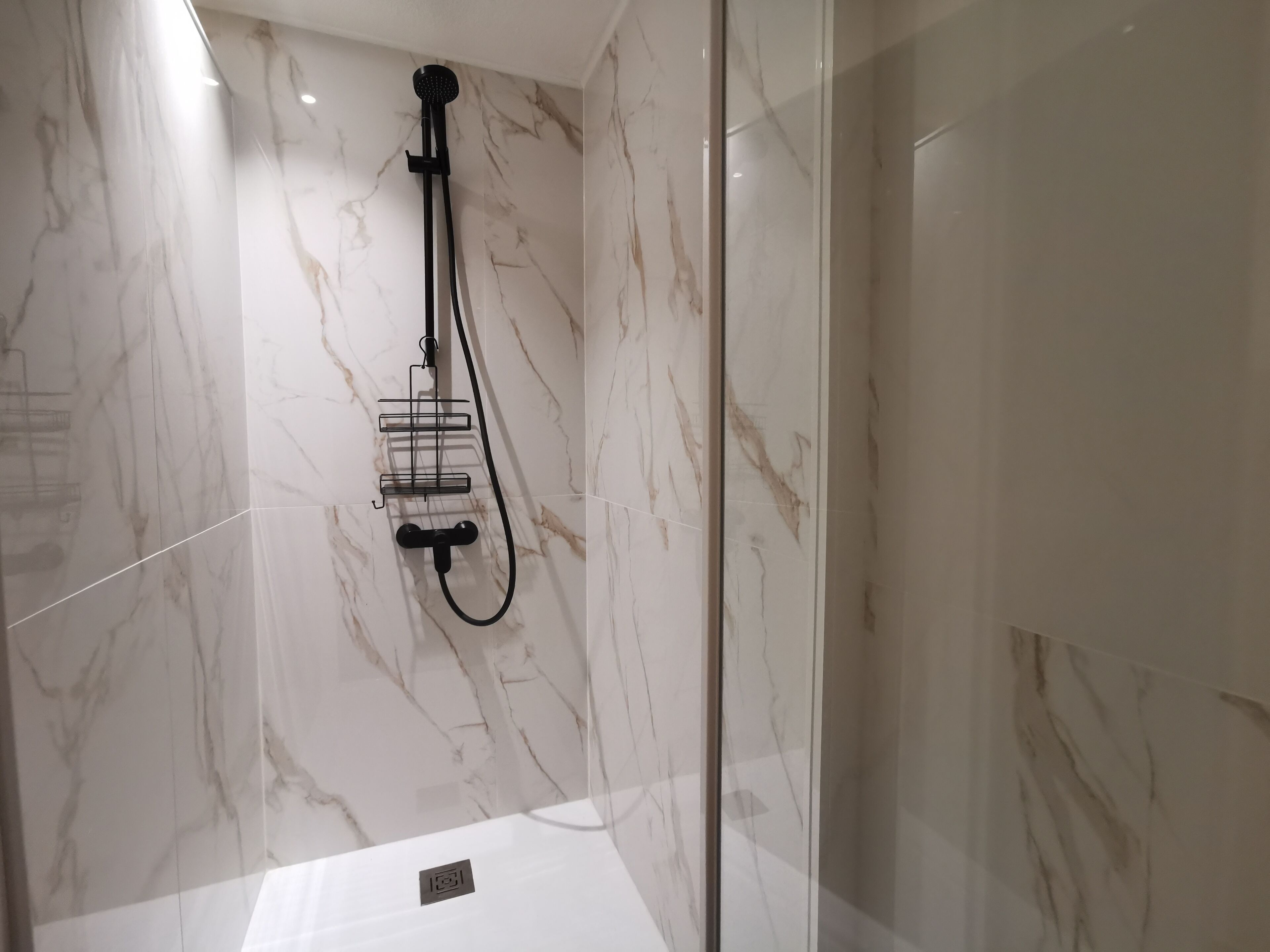 A modern bathroom with a glass-enclosed shower, marble walls, and a black showerhead.