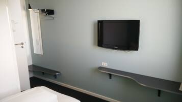 Une chambre d’hôtel avec un lit, un téléviseur fixé au mur, une table de chevet et une lampe.