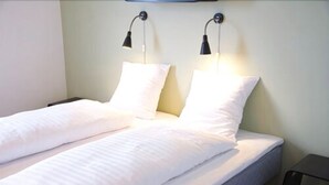 A twin bed with white bedding and two wall-mounted reading lamps. - Motel X (Randers)