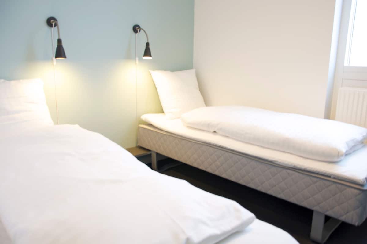 Habitación doble con dos camas, una mesita de noche y una lámpara fijada a la pared.