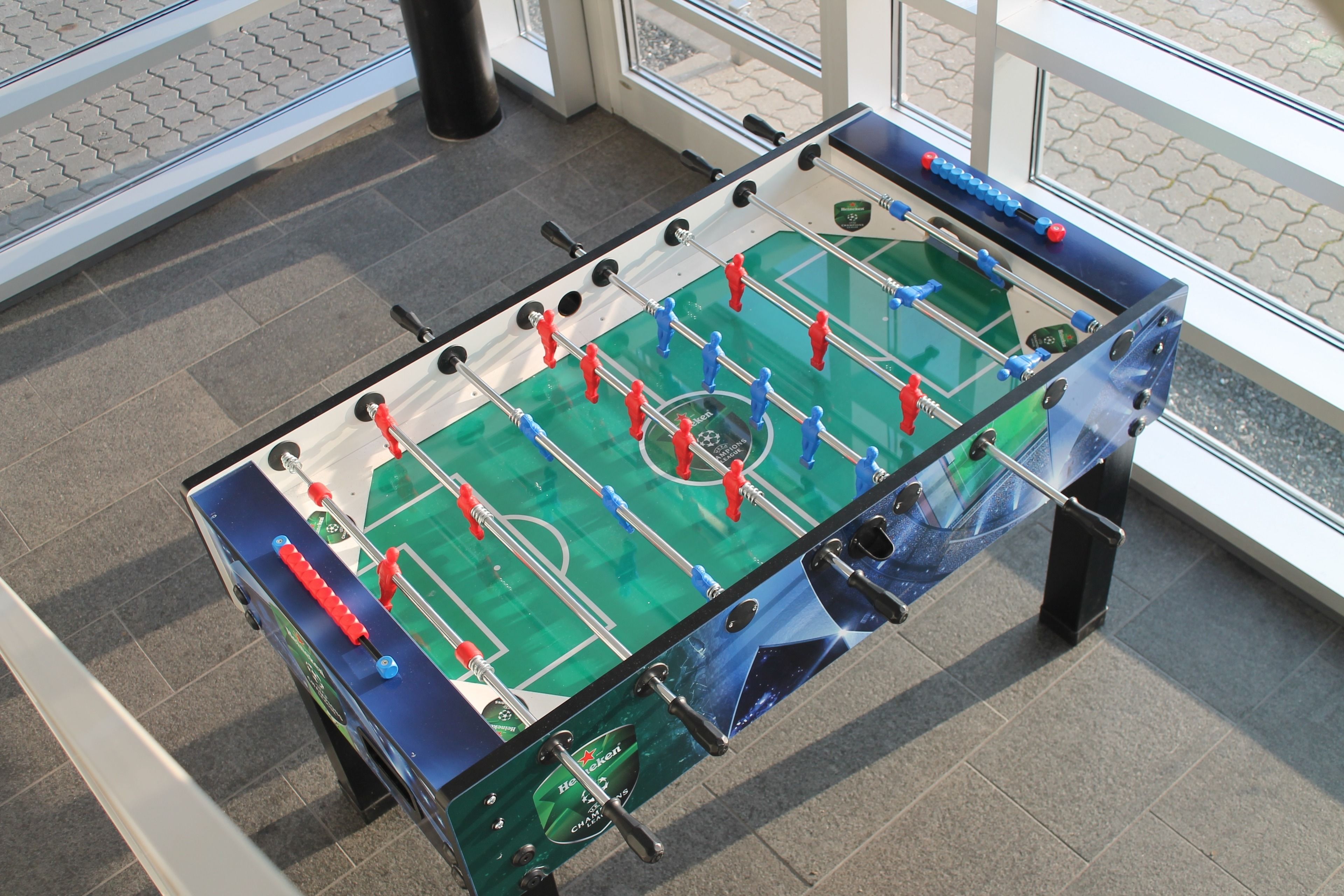Una taula de futbolí a una habitació amb terra de rajola i finestrals amplis.