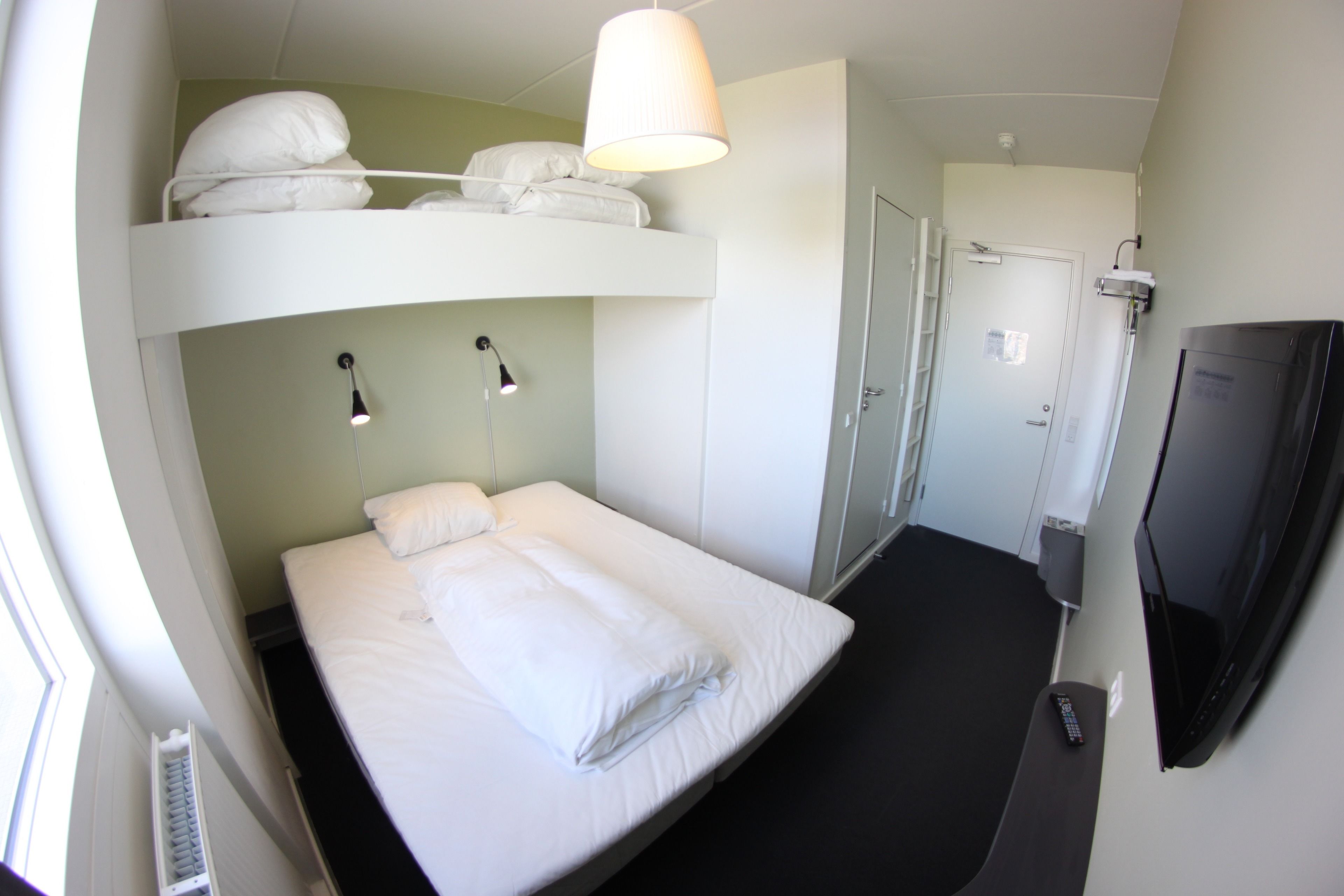 Een slaapkamer met een stapelbed, een televisie, een bureau en een deur.