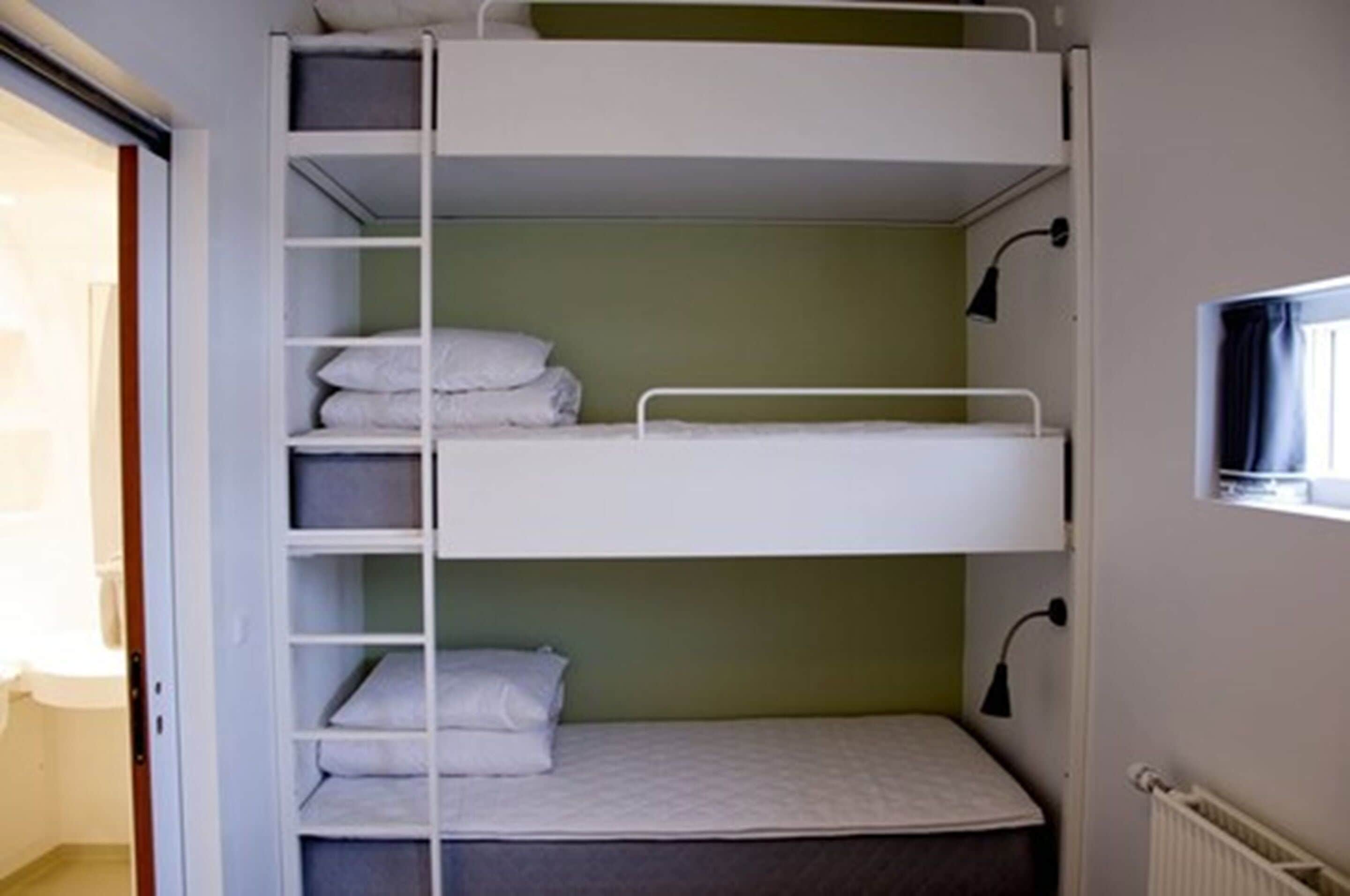 A bunk bed with a shelf above and a desk lamp beside it.