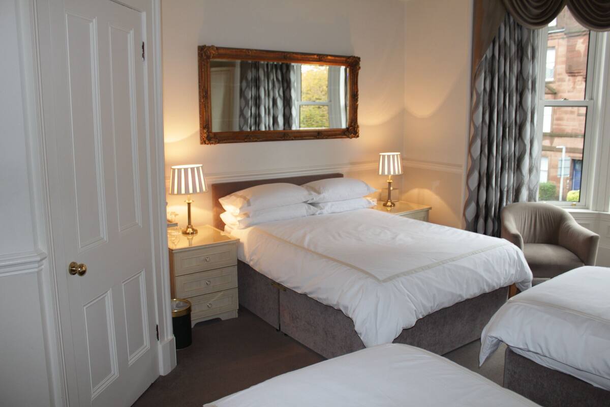 A hotel room with a large bed, bedside lamps, a chair, and a window with curtains.