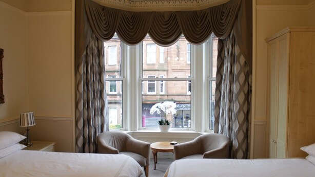 Ein Hotelzimmer mit zwei Betten, einem kleinen Tisch und einem Fenster mit Vorhängen.