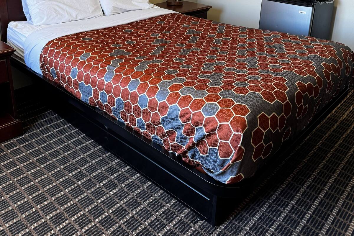 A hotel room with a bed, a nightstand, a lamp, a microwave, and a framed picture on the wall.