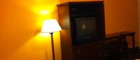 A hotel room with a bed, a dresser, a lamp, and a television.