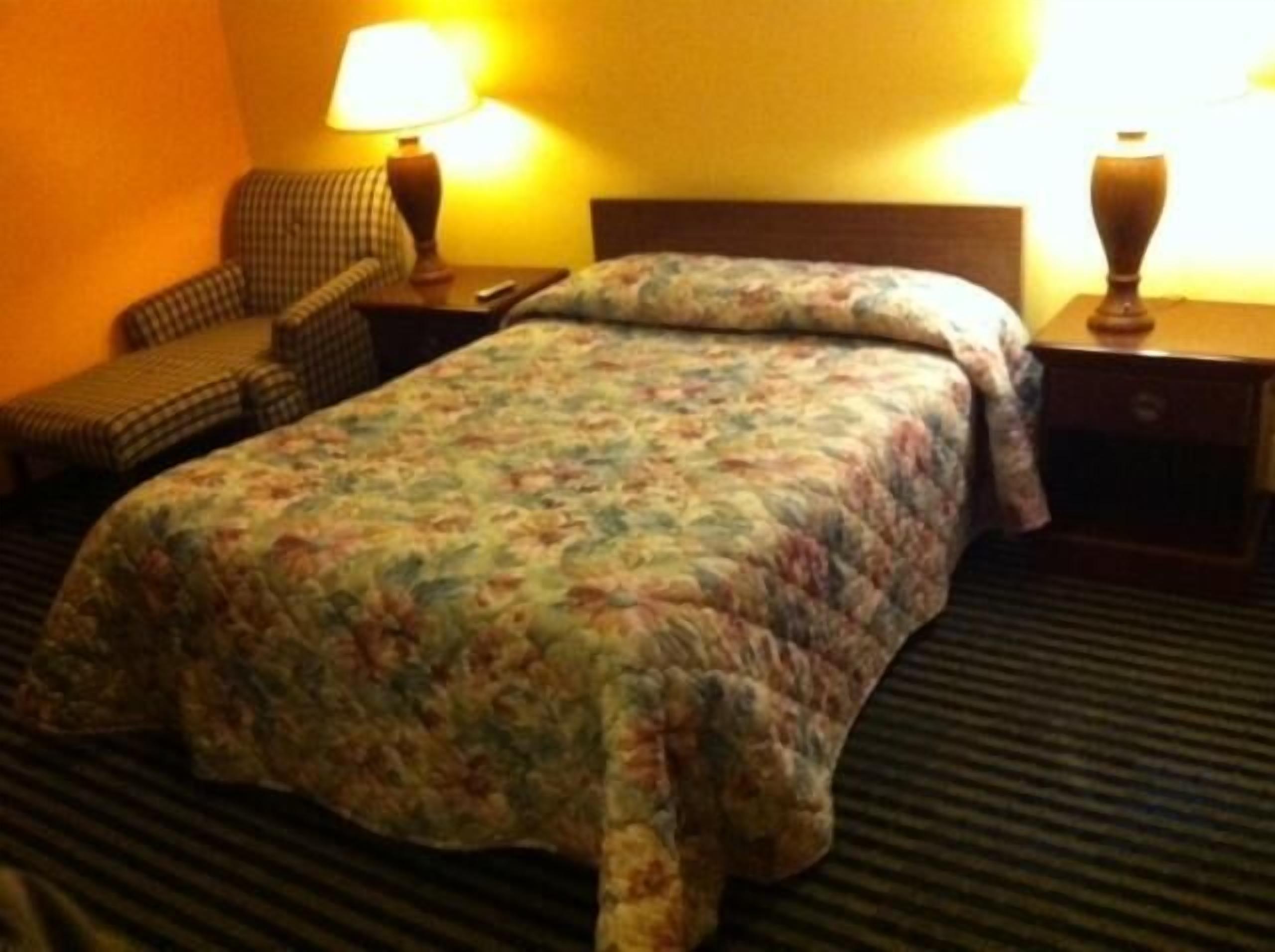 Una habitación de hotel con una cama, una silla, dos mesitas de noche y lámparas.