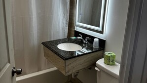 A bathroom with a white toilet, a sink with a mirror above it, and a shower curtain. - Ashford Motel (Ashford)