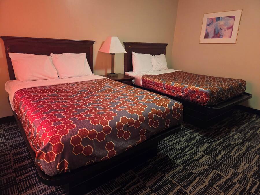 Two double beds with patterned bedspreads, a nightstand with a lamp, and a framed picture on the wall.