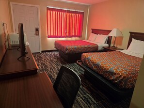 A hotel room with two beds, a desk with a computer, a lamp, and a window with red curtains. - Ashford Motel (Ashford)