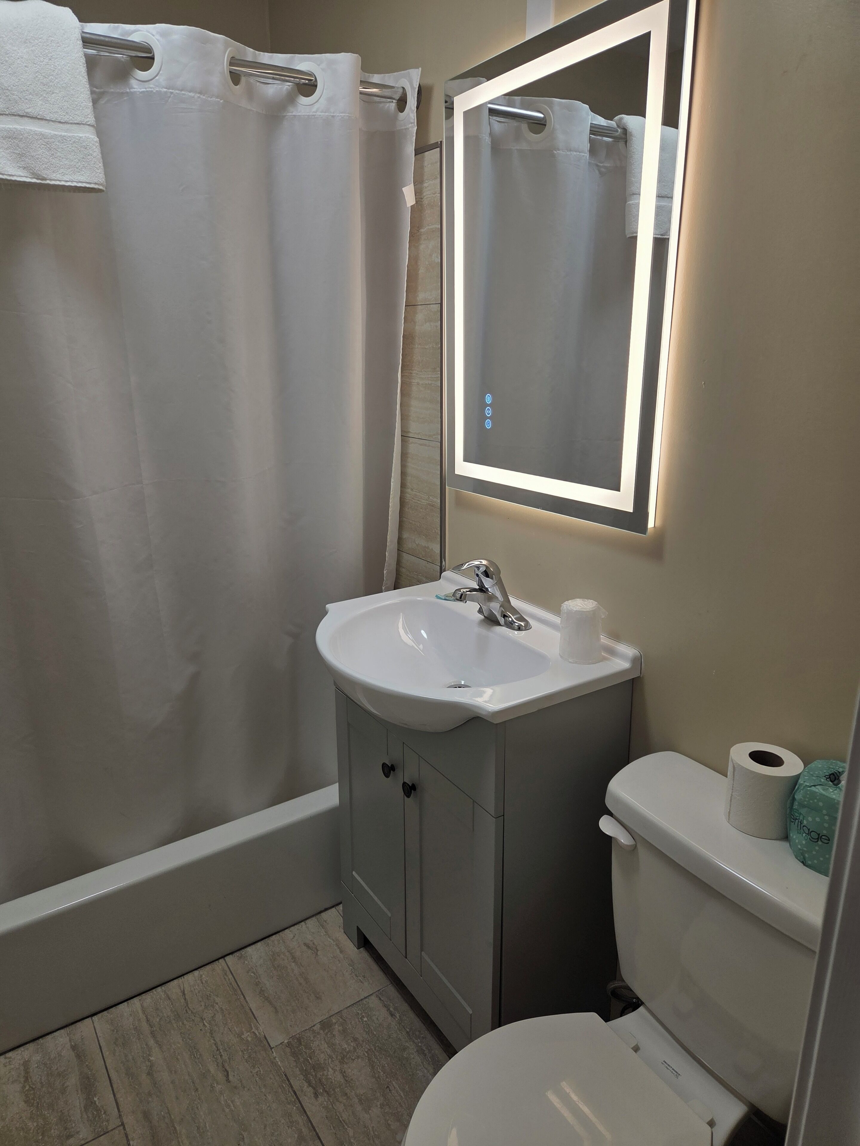 A bathroom with a shower, sink, mirror, toilet, and a towel rack.