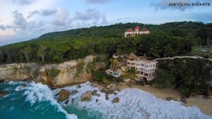 Une propriété située sur la côte, avec un grand bâtiment entouré d’une végétation luxuriante et de falaises rocheuses.
