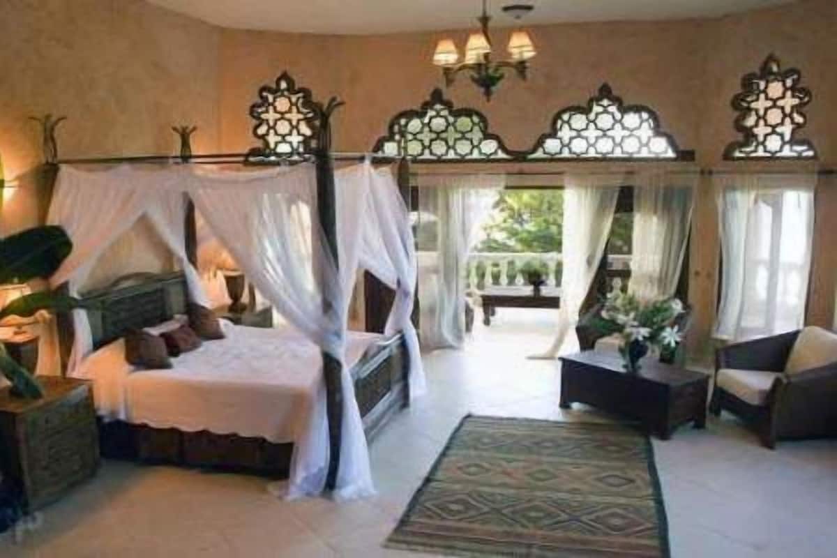 Ein Schlafzimmer mit einem Himmelbett, einem Nachttisch, einem Sessel und Blick ins Freie.