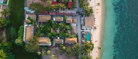 An aerial view of a resort with multiple bungalow-style buildings, a beach, and a pool area.