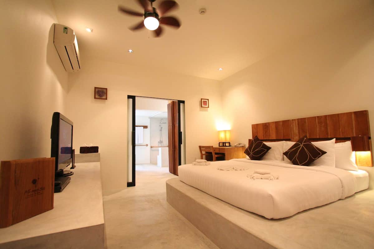 Une chambre d’hôtel avec un grand lit, une télévision, un bureau et un ventilateur de plafond.