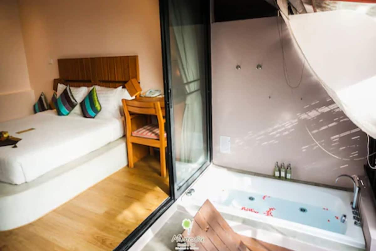 Une chambre d’hôtel avec un lit, une chaise en bois, une porte en verre et une baignoire.
