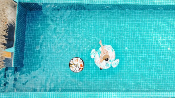 A top-down view of a swimming pool with clear blue water, a tiled edge, and a small inflatable float with a person lying on it. - Mimosa Resort & Spa (Koh Samui)