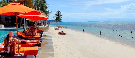 Rannalla, valkoista hiekkaa, aurinkotuoleja, aurinkovarjoja