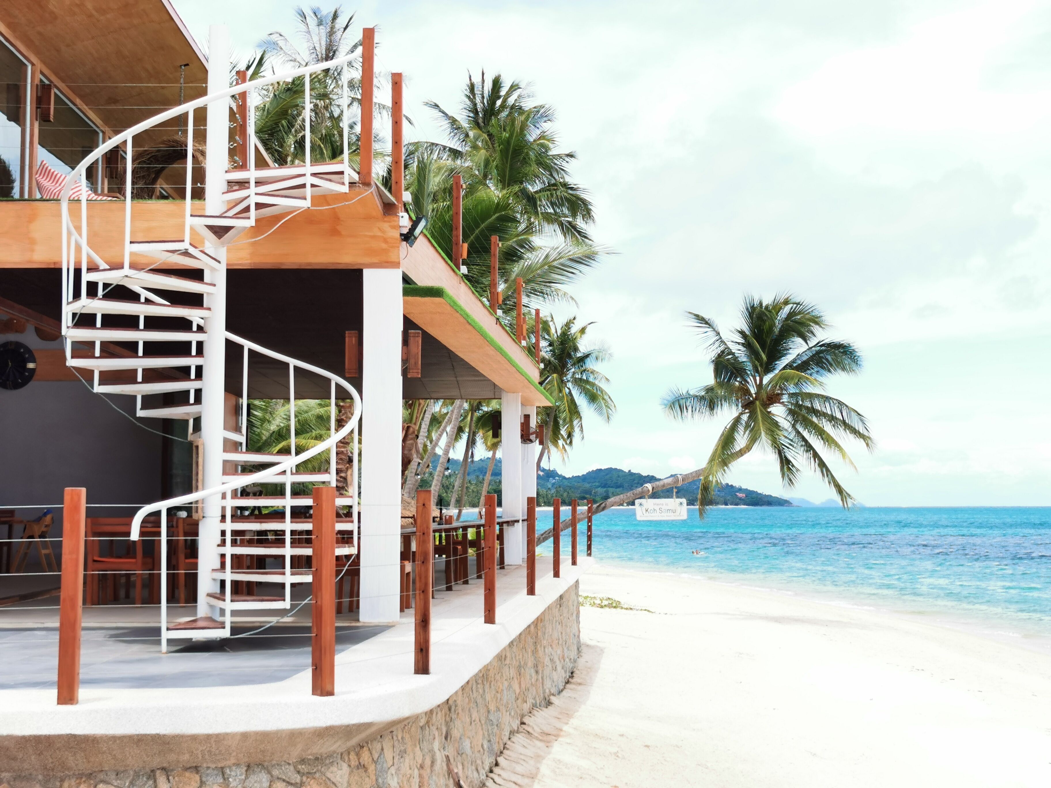 Ein Strandhotel mit einer Wendeltreppe, Palmen und Blick auf den Ozean.
