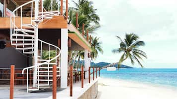 Un hotel frente a la playa con una escalera espiral, palmeras y vistas al océano.