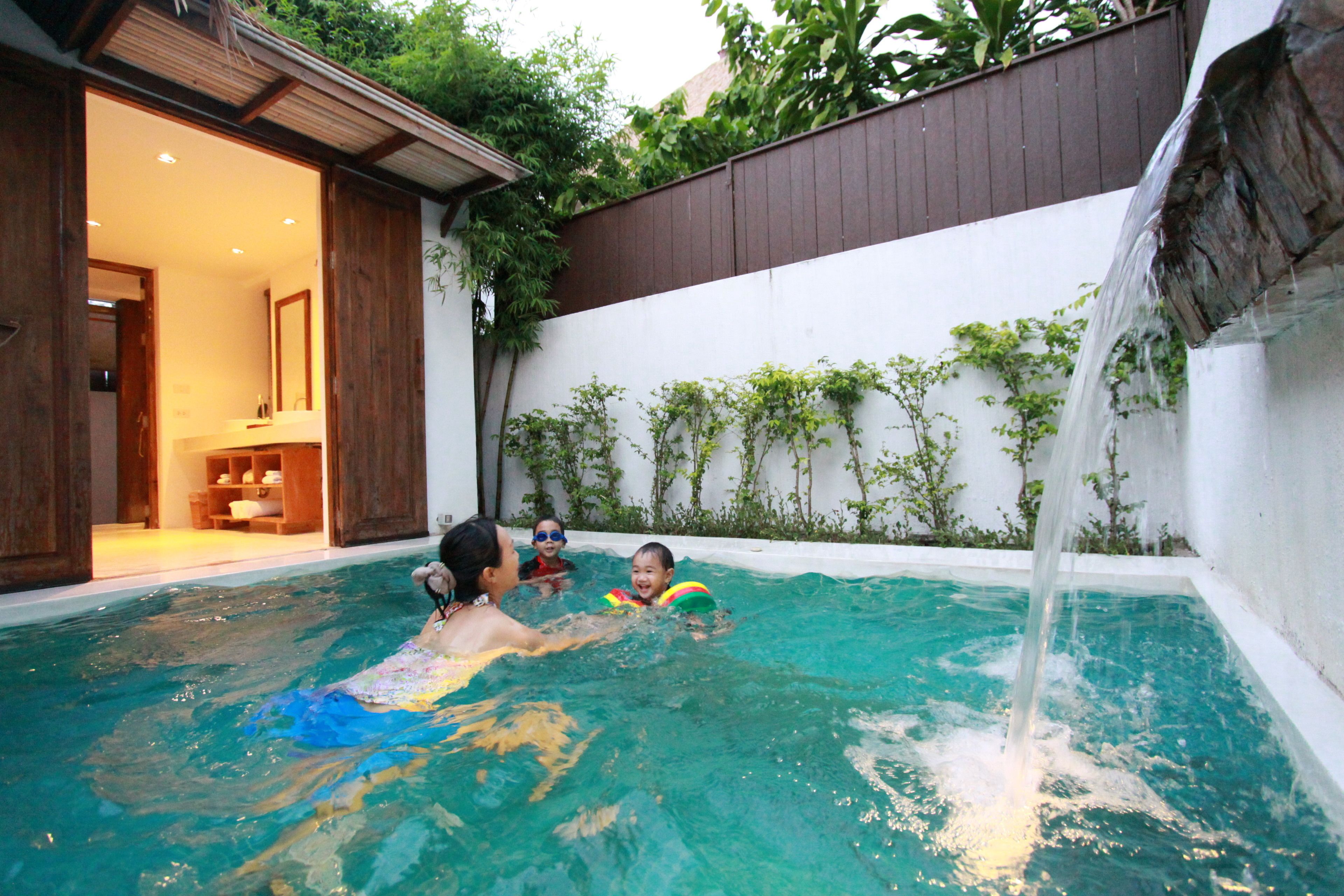 A swimming pool with clear water, a wooden deck, and a white wall with climbing plants.