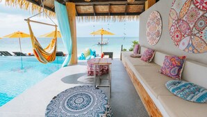 A poolside area with a hammock, lounge chairs, and a table with a chair. There are colorful cushions on a sofa and a patterned rug on the floor. - Mimosa Resort & Spa (Koh Samui)
