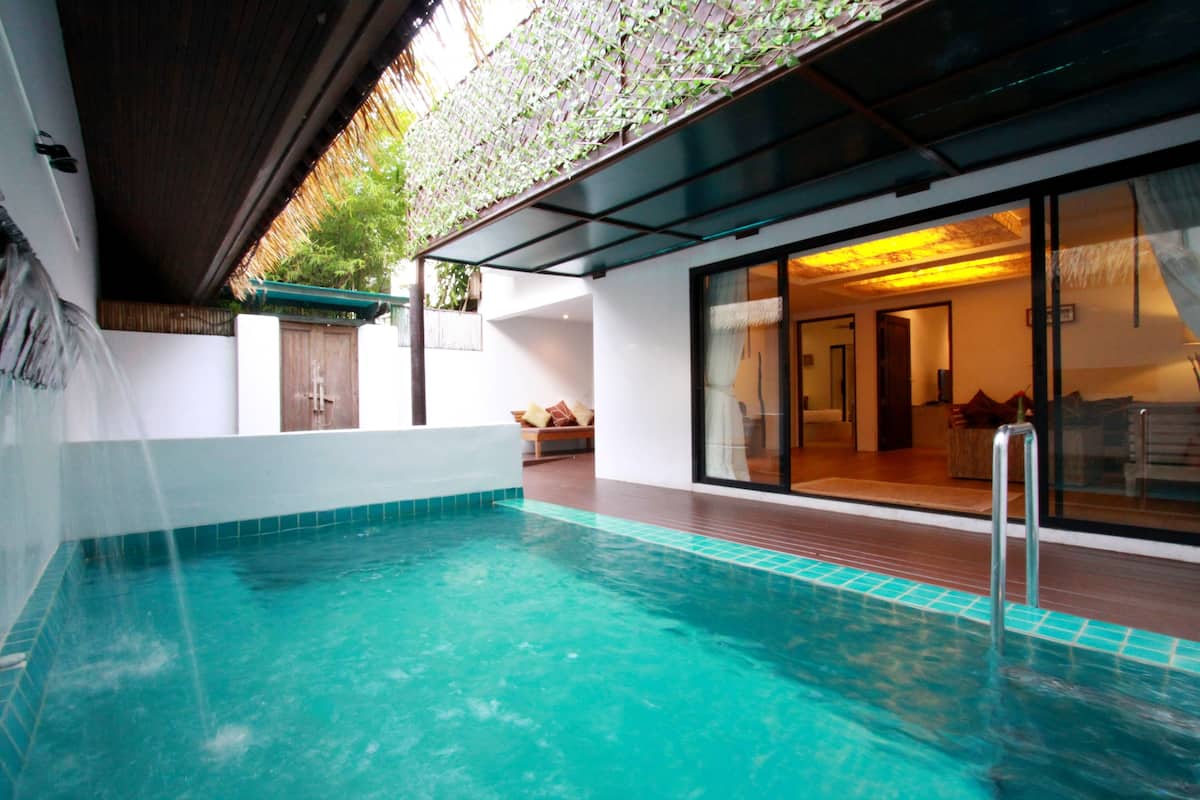 Un espace piscine intérieur moderne offrant une vue dégagée sur le salon attenant, qui comprend un canapé et une porte vitrée donnant sur une pièce bien éclairée.
