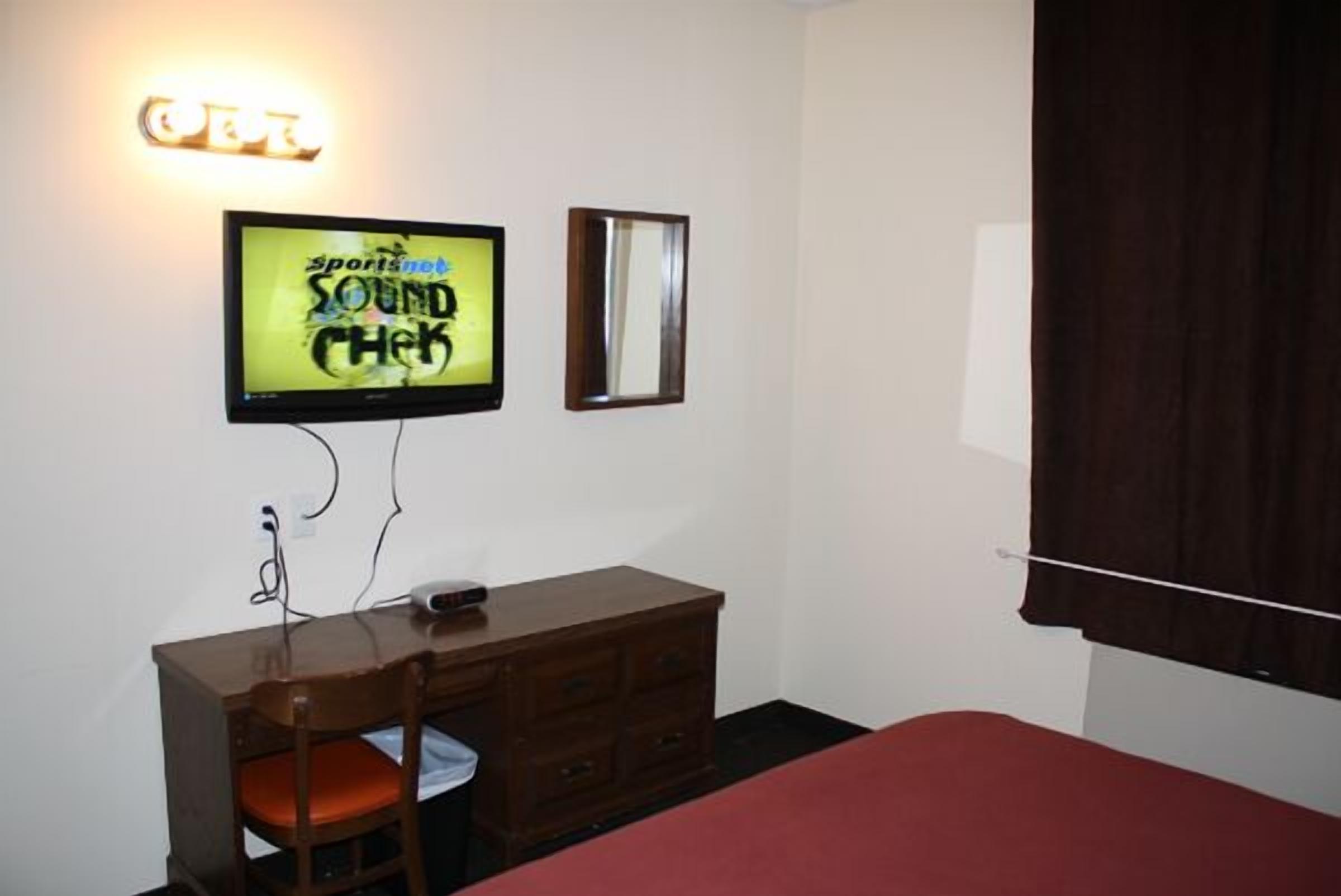Una habitación con una cama, un aparador de madera, un televisor montado en la pared y un espejo.