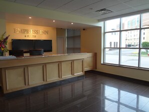 A reception area with a counter, a TV, and a window with a view of buildings. - Empress Inn and Suites by The Falls (Niagara Falls)
