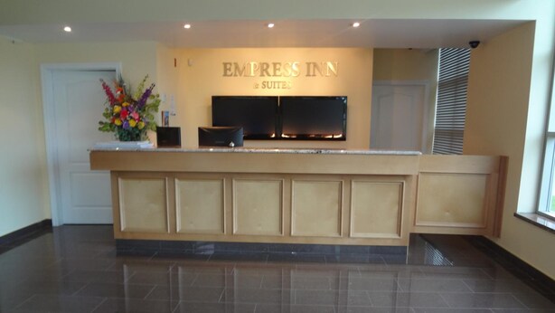 Un mostrador de recepción con un televisor de pantalla plana, un arreglo floral y un letrero que dice 'EMPRESS INN & SUITES'.