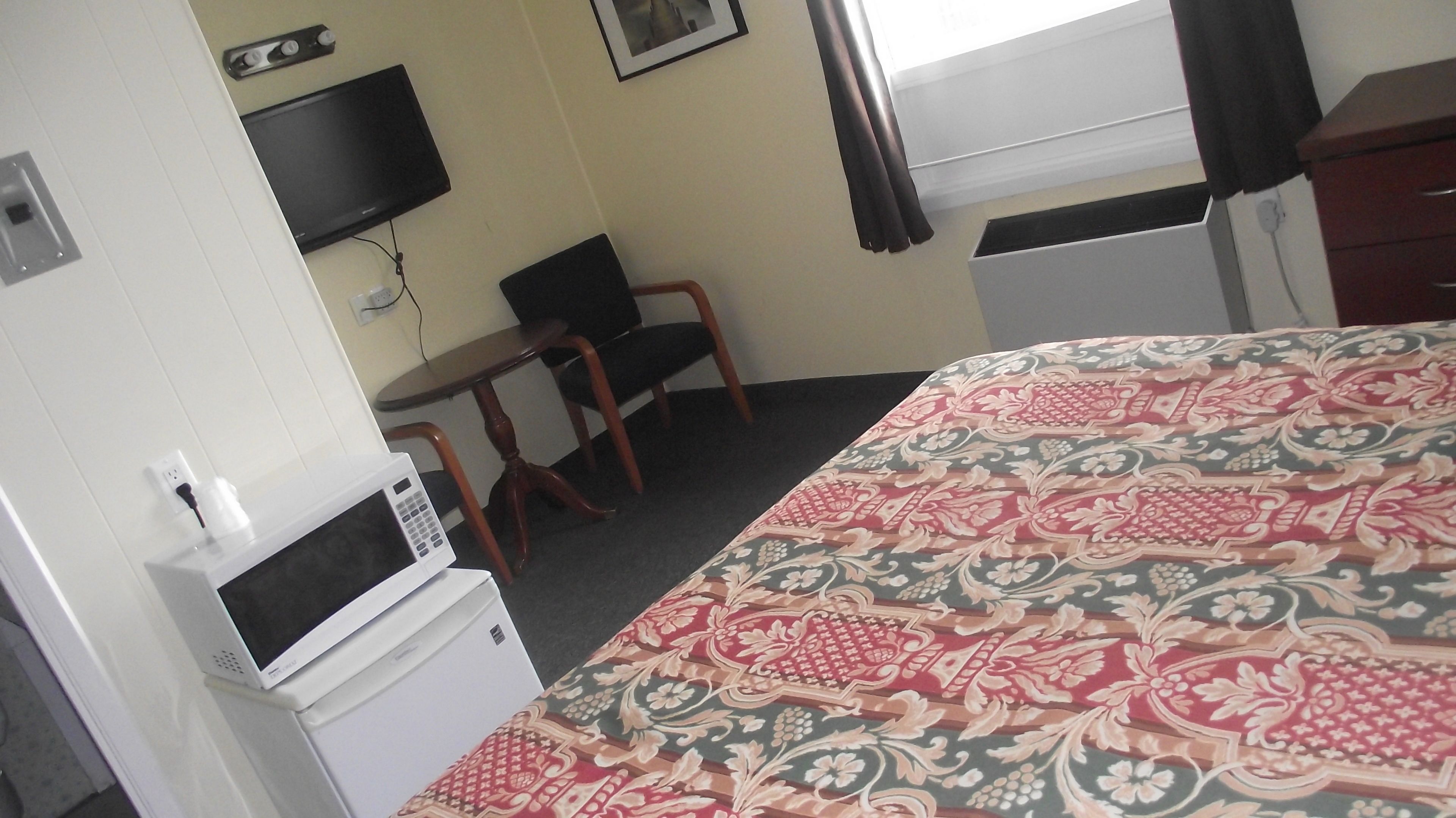 Une chambre d’hôtel équipée d’un lit, d’un bureau, d’une chaise, d’une télévision et d’un four à micro-ondes.