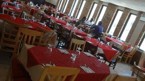 Un comedor amplio con varias mesas cubiertas con manteles rojos, sillas de madera y grandes ventanales que dejan entrar luz natural.