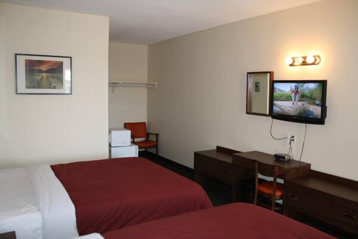 A hotel room with two beds, a desk, a chair, a TV, and a mirror.