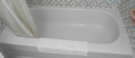 A bathroom with a white bathtub, a white towel, and patterned tiles.