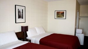 Una habitación de hotel con dos camas, una mesita de noche, una lámpara y dos cuadros en la pared.