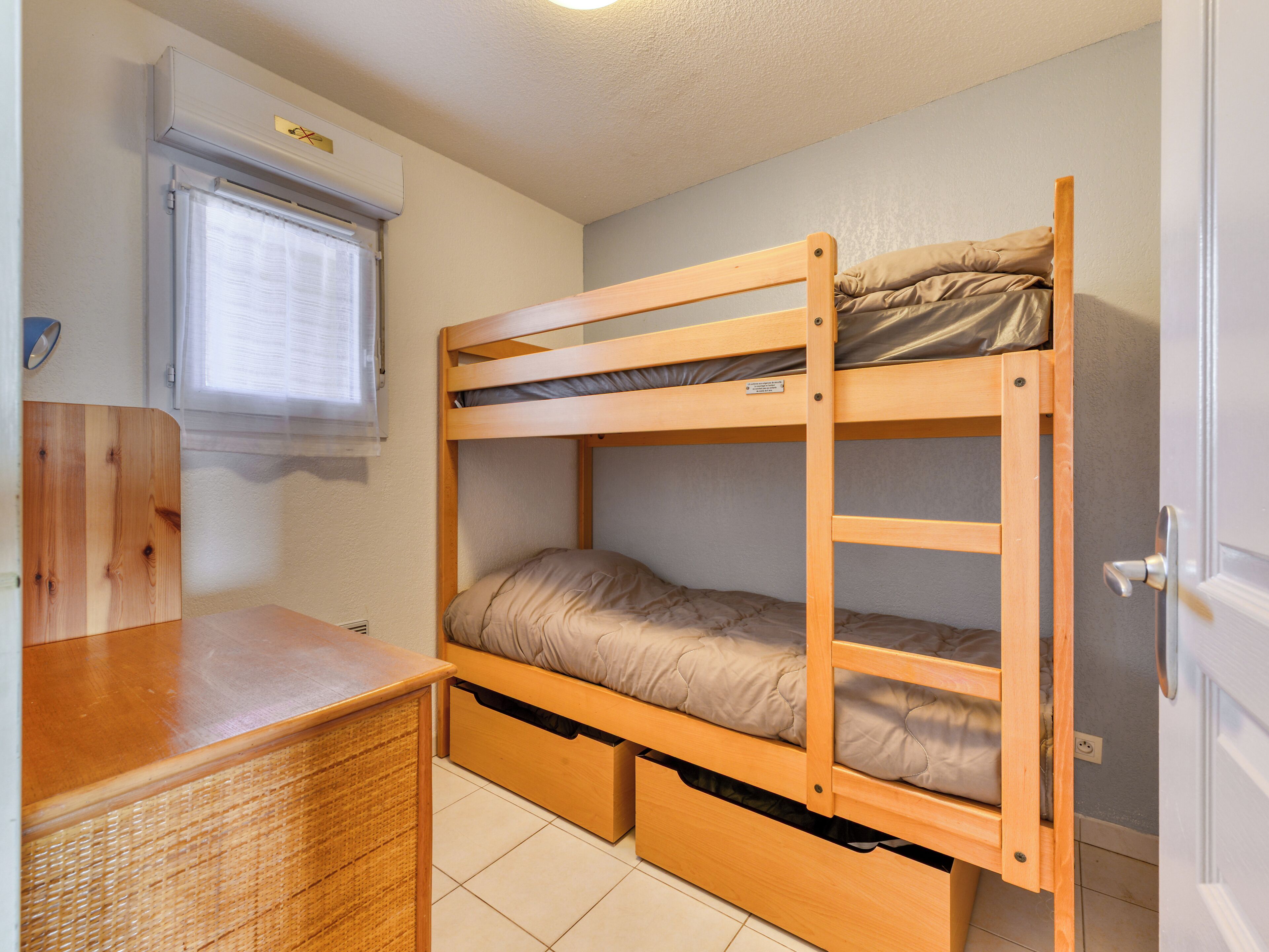 A bunk bed with a desk and drawers, a window with blinds, and a door.