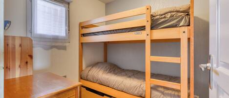 A bunk bed with a desk and drawers, a window with blinds, and a door.