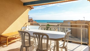 Un balcón con mesa y sillas, con vista a una playa y al mar.