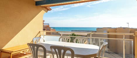 A balcony with a table and chairs, overlooking a beach and the sea.