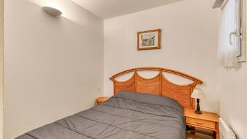 Un dormitorio con cama, mesita de noche, lámpara, un cuadro enmarcado en la pared y una ventana con cortinas.