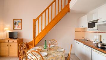 A kitchen with a wooden staircase, a dining table set with plates and glasses, a television on a cabinet, and a microwave above the counter.