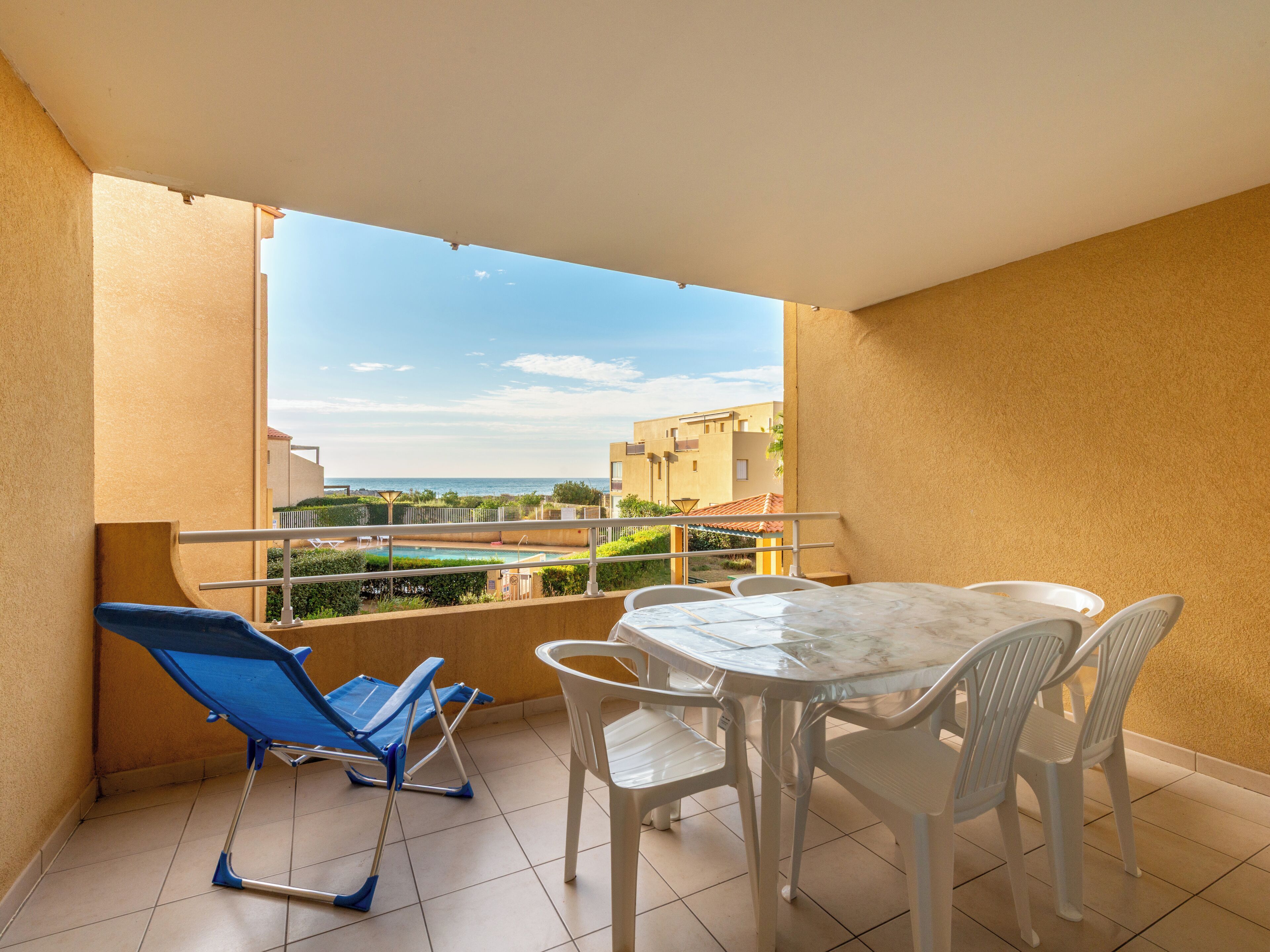 A balcony with a table and chairs, a blue chair, and a view of buildings and a pool.